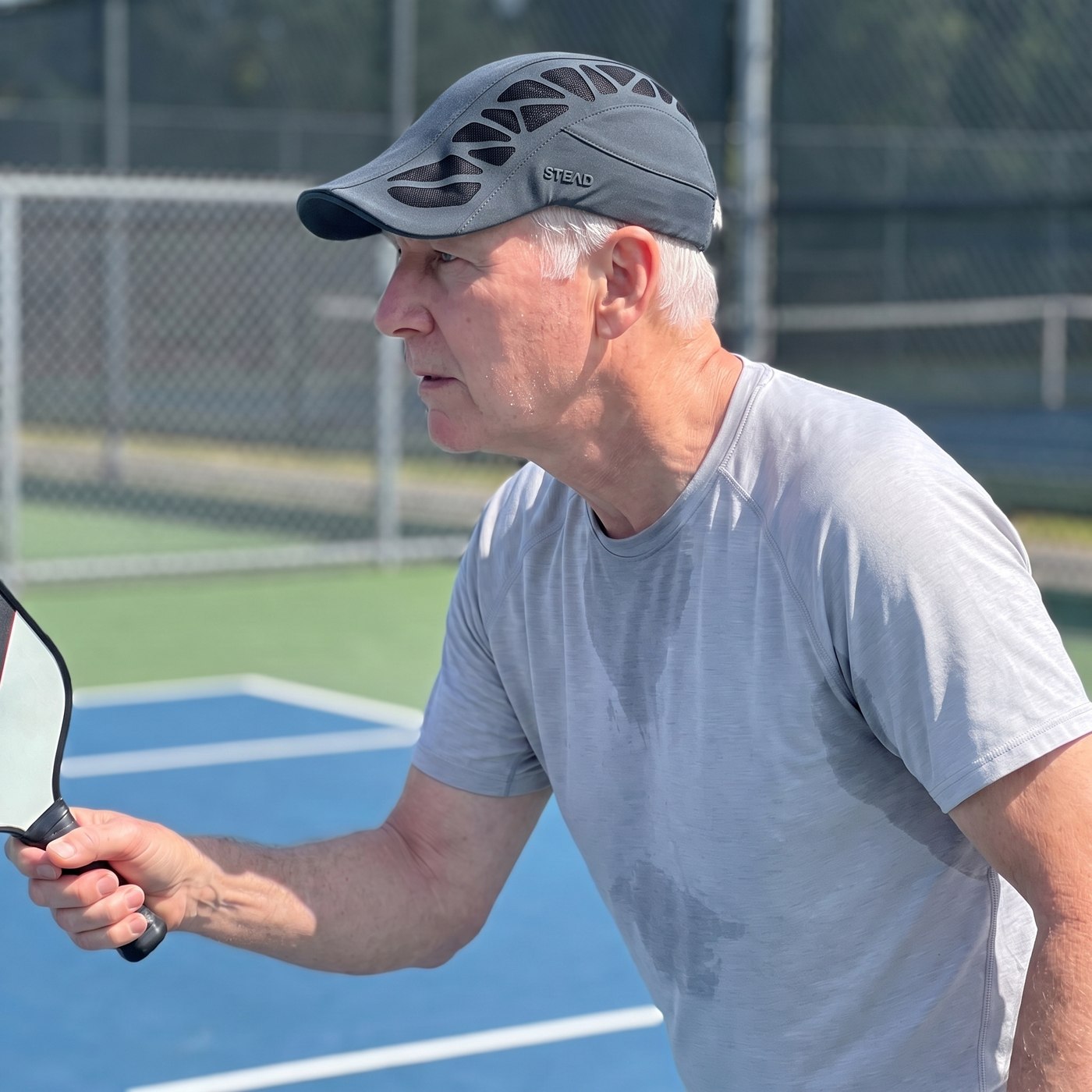 A man in the Aeromesh Evo Cap playing pickleball on a sunny court, his shirt damp with sweat