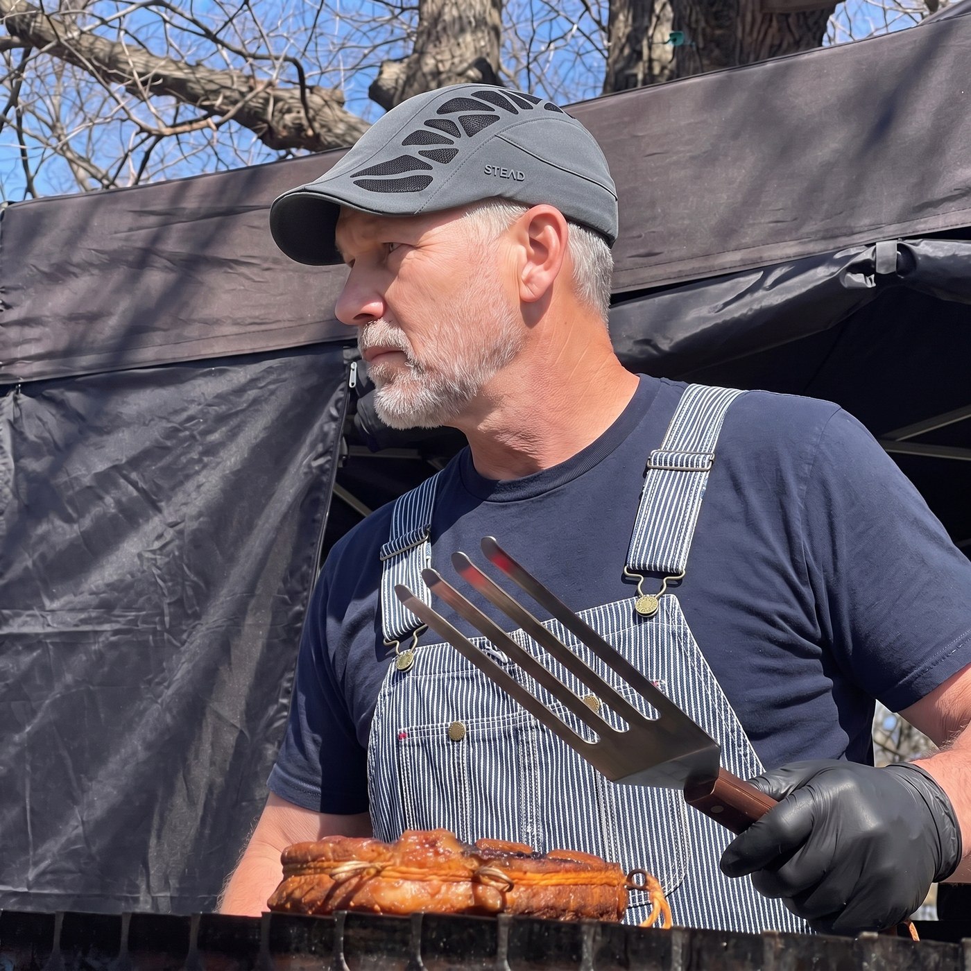 A man in the Aeromesh Evo Cap at his smoker, in profile, a big fork in his gloved hand